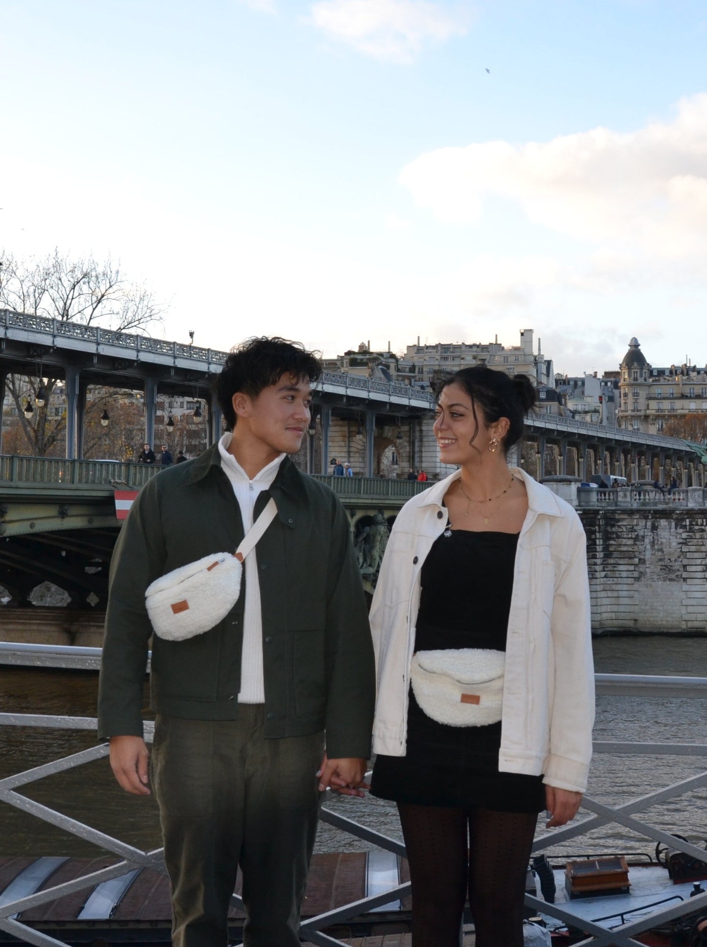 Jeune femme brune et jeune homme brun sur les quais de bord de seine parisien portant un Sac banane Binette Boule de neige en molleton blanc upcyclé fabriqué à partir de chutes de tissus dormants voués à être jetés ou brûlés et revalorisé par la marque française Binette qui fabrique des sacs banane et accessoires upcyclés tendance, pratiques, durables, éthique, écoresponsable avec un impact environnemental réduit et en luttant contre le gaspillage textile.