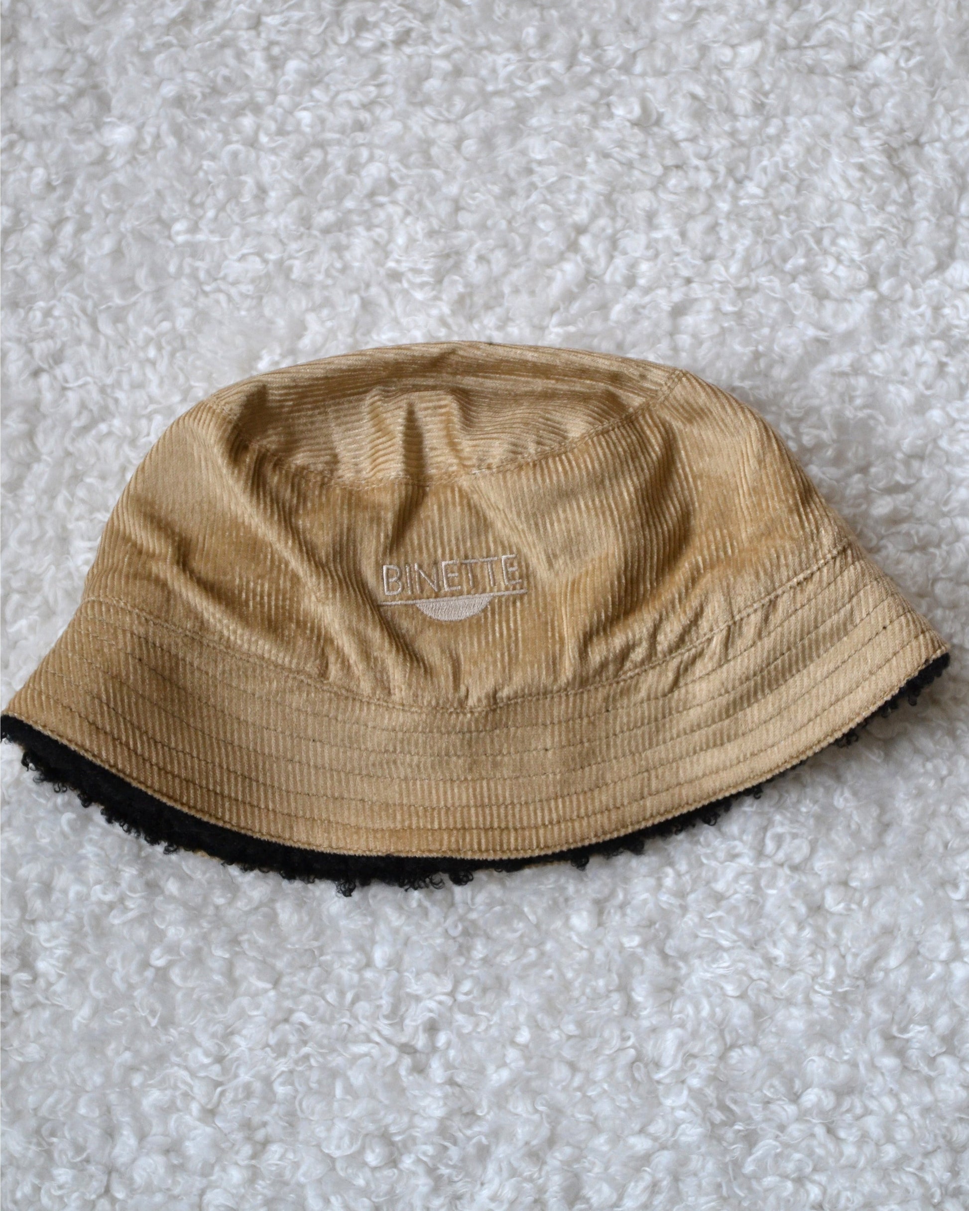 Packshot du bob réversible Binette, montrant les deux côtés distincts : un velours côtelé beige au style épuré et une moumoute noire chaleureuse. Un accessoire écoresponsable en tissu upcyclé, parfait pour affronter l’hiver avec élégance et conscience écologique.