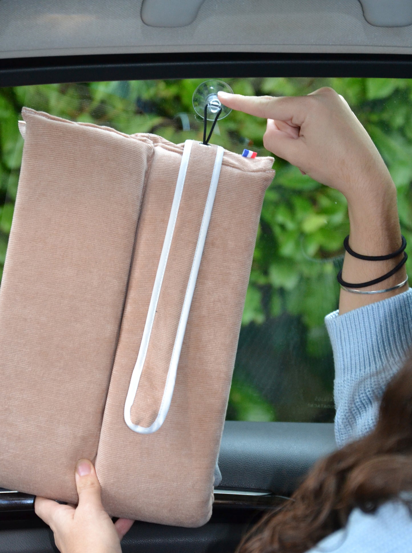 Coussin rose de voyage utilisation multiple. La modèle colle le coussin rose sur la vitre grâce à la ventouse et peut dormir dessus pendant le trajet en voiture.