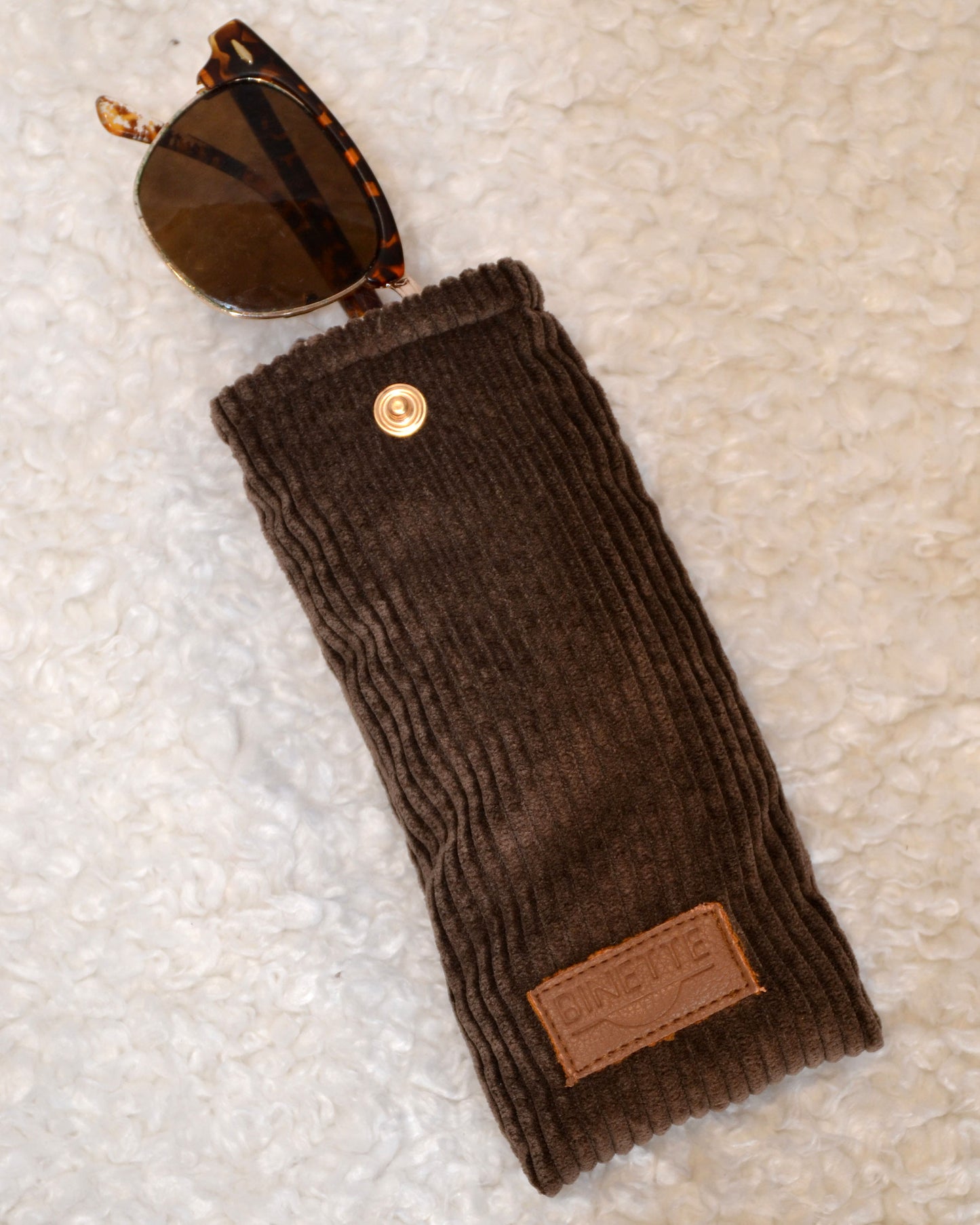 Étui à lunette marron chocolat en velours côtelé avec lunette de soleil rentrée.