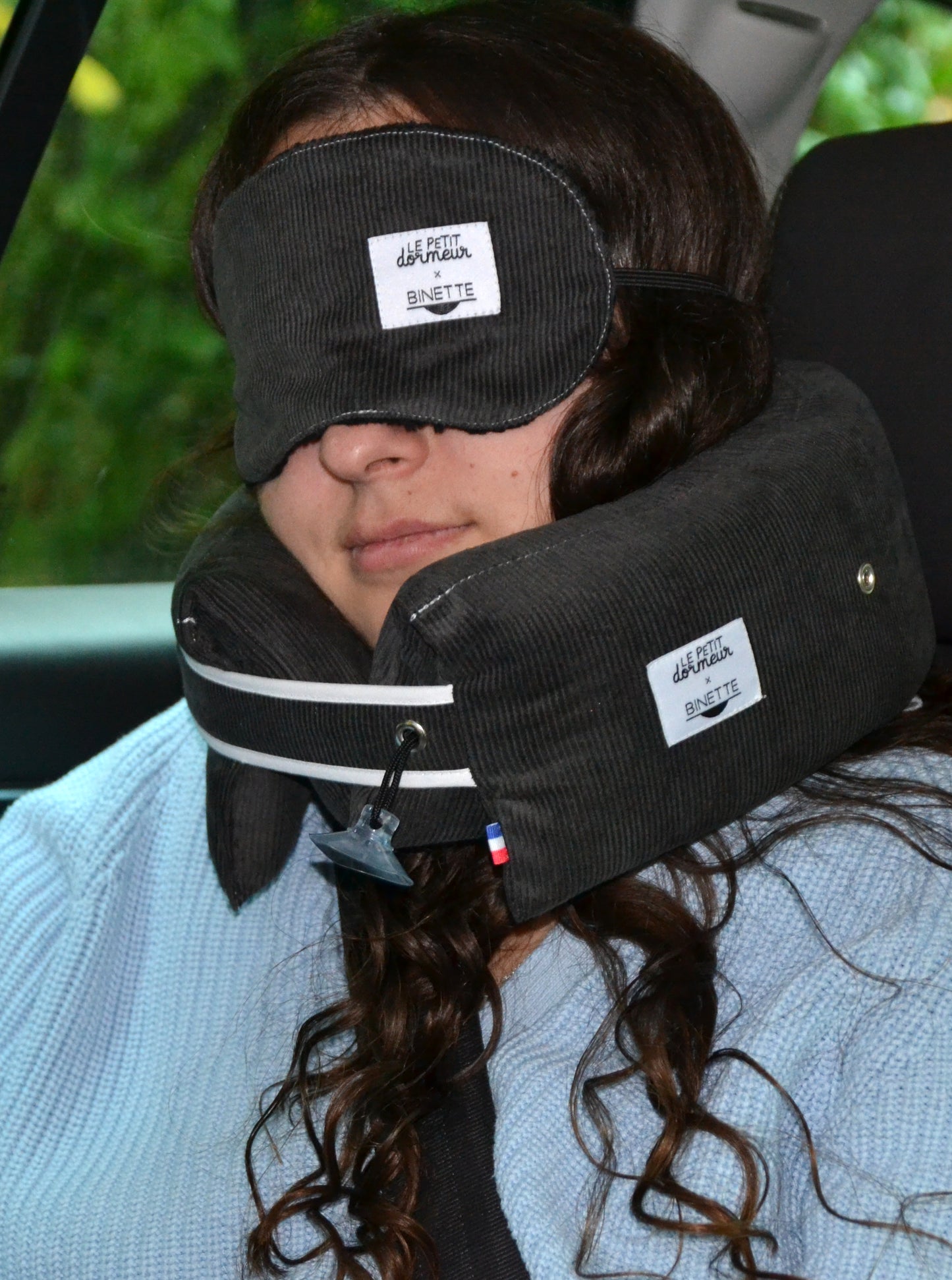 Modèle dormant et portant le masque de sommeil et le coussin de voyage ergonomique en velours côtelé gris foncé clair lors d'un trajet en voiture.
Cet ensemble est conçu pour un confort optimal tout en respectant l’environnement.