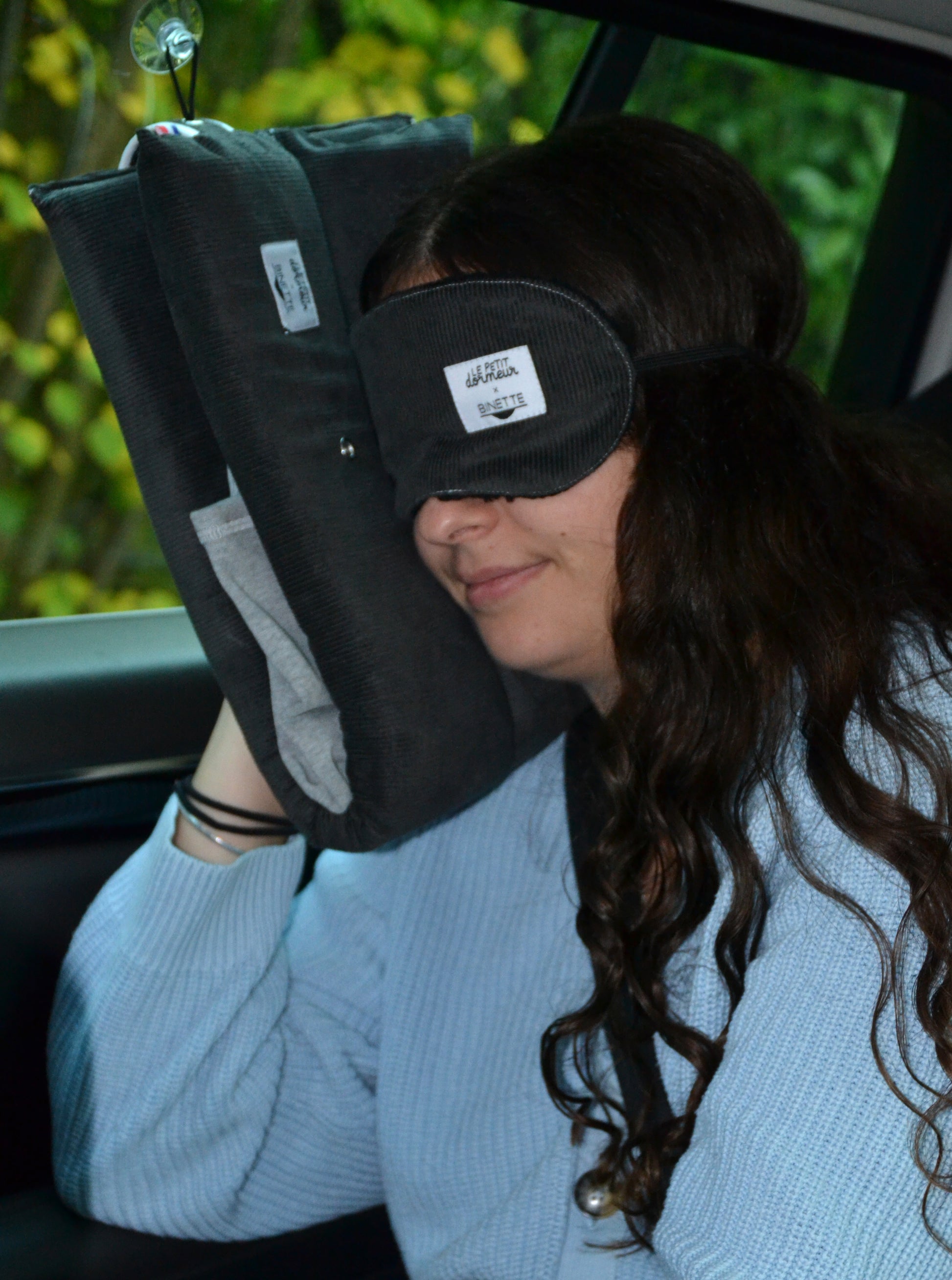 Modèle portant le masque de sommeil sur les yeux et le coussin de voyage ergonomique en velours côtelé gris lors d'un trajet en voiture. 
Cet ensemble est conçu pour un confort optimal tout en respectant l’environnement.
