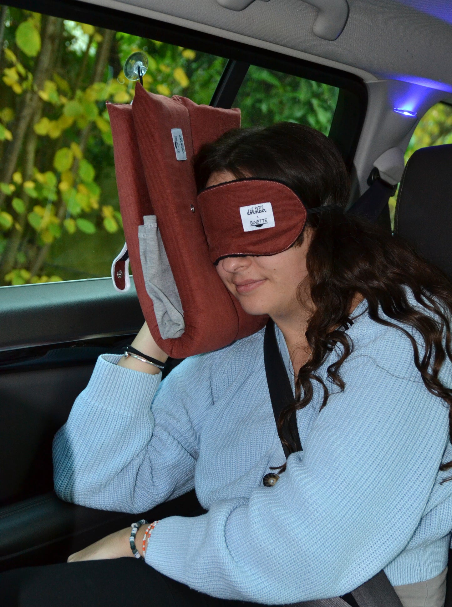Modèle portant le masque de sommeil sur les yeux et le coussin de voyage ergonomique en velours côtelé rouge lors d'un trajet en voiture.
Cet ensemble est conçu pour un confort optimal tout en respectant l’environnement.