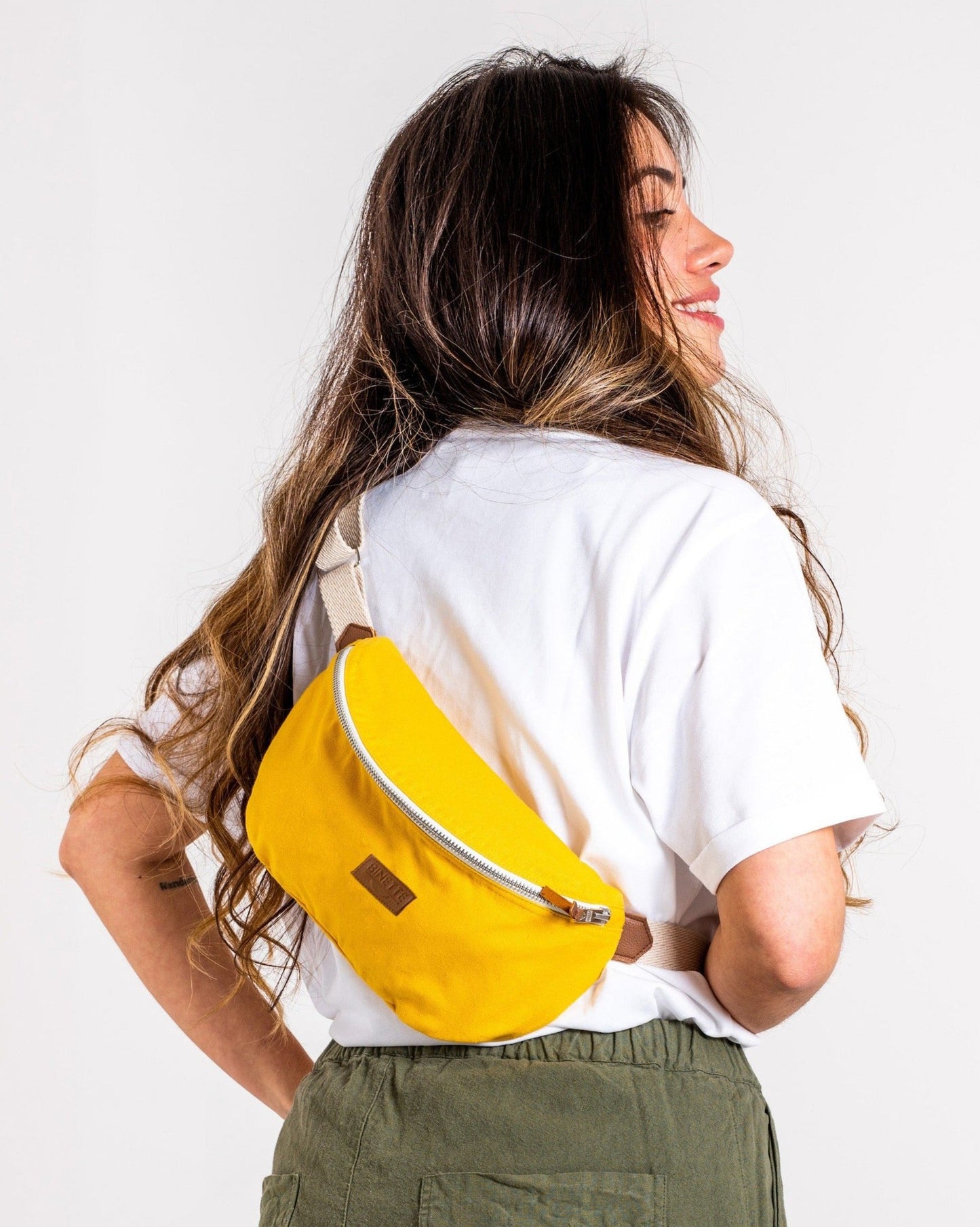 Jeune femme brune portant un Sac banane Binette upcyclé à partir de chutes de tissus dormants voués à être jetés ou brûlés revalorisés par Binette la marque française écoresponsable de sacs banane et accessoires écoreponsables, éthiques, tendances, jolis, ecoresponsable, avec un faible impact environnemental et luttant contre le gaspillage textileécoresponsable pour un sac banane upcyclé jaune collection binette x perus