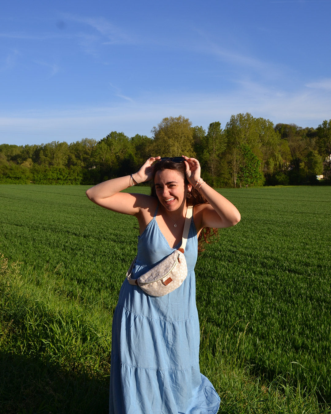 Dans cette scène ensoleillée, une femme radieuse porte la Binette Marguerite Beige en bandoulière, illustrant parfaitement la combinaison de liberté et d'élégance qu'offre ce sac. Son sourire lumineux témoigne du confort et de la praticité de cet accessoire, lui permettant de se déplacer en toute aisance tout en gardant l'essentiel à portée de main. La Binette Marguerite Beige devient ainsi le compagnon idéal pour une journée remplie d'aventures estivales.