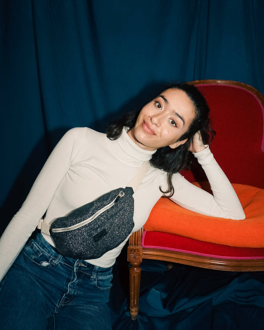 Jeune femme brune regardant la caméra avec son sac banane upcyclé Disco sangle noire en tissu noir gris pailleté fabriqué par une marque française écoresponsable Binette. 
Mode éthique quais parisiens mode responsable tissu upcyclé chutes de tissus dormants voués à être jetés ou brûlés accessoires upcyclés pratiques tendances et éco-friendly