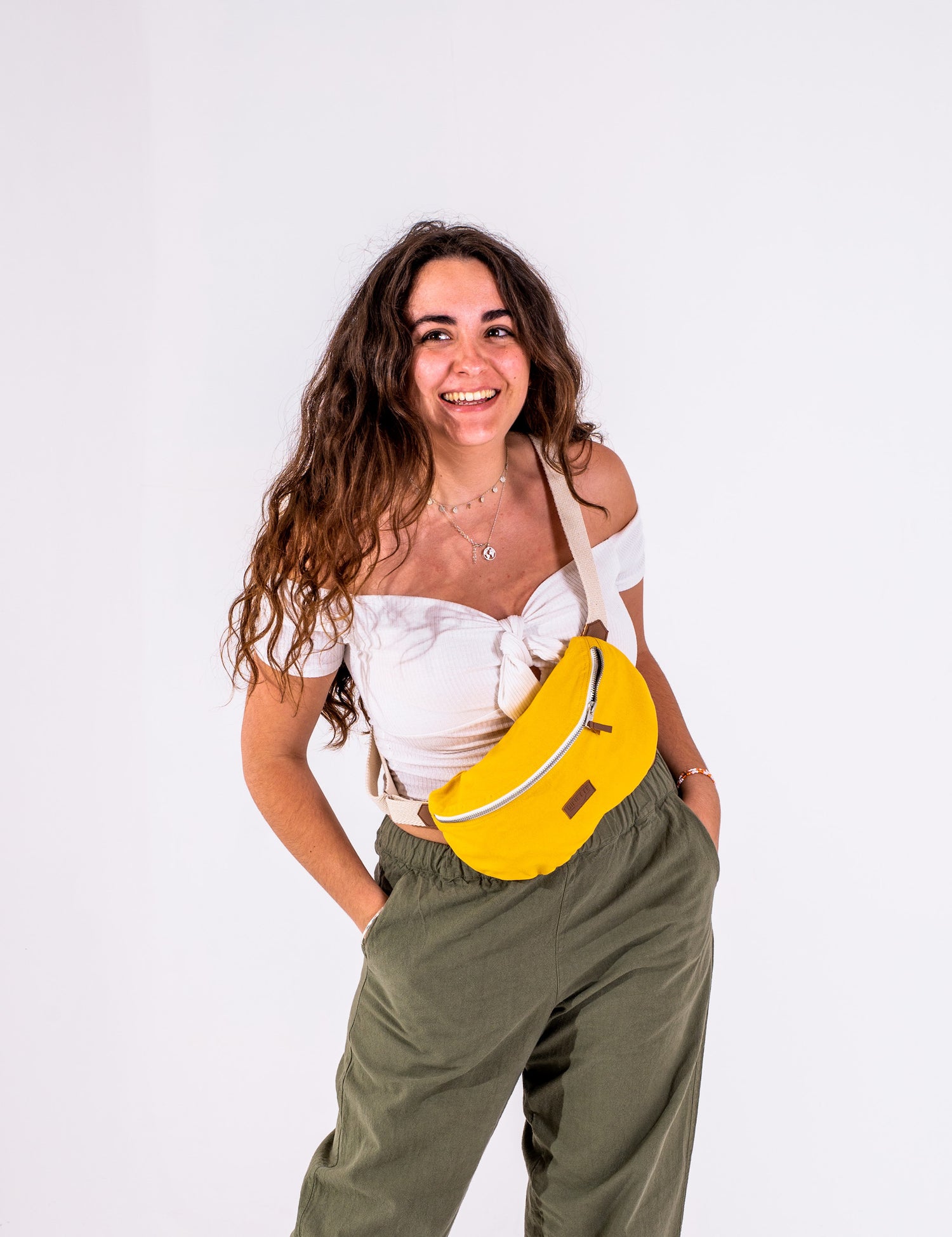 Photo de Pénélope Chapuis la dirigeante de Binette qui porte un sac banane jaune et un pantalon vert sur un fond blanc. 