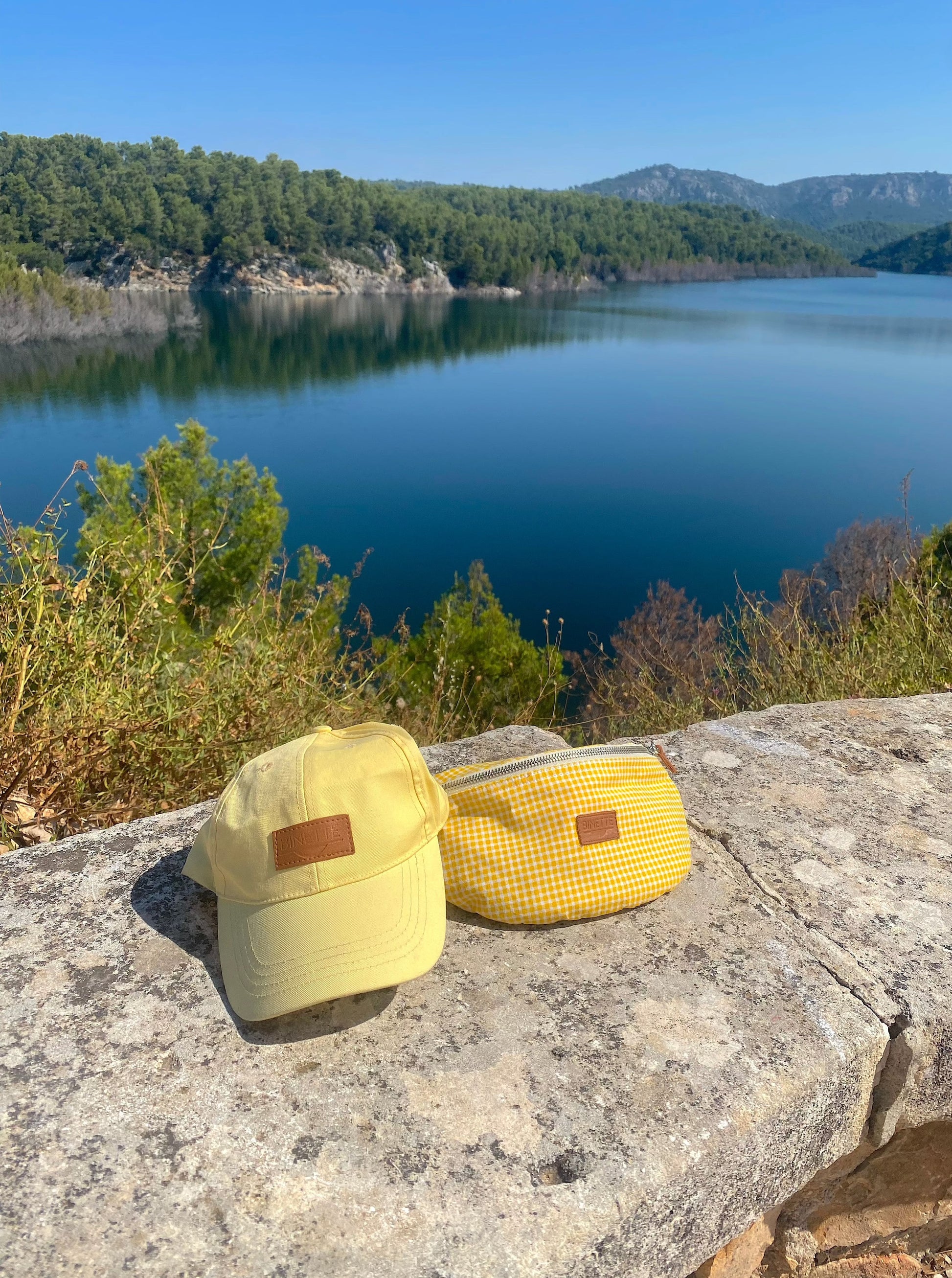 une casquette jaune et un sac banane jaune vichy fabriqués en matière éco-responsable photo prise au bord d'un lac en été