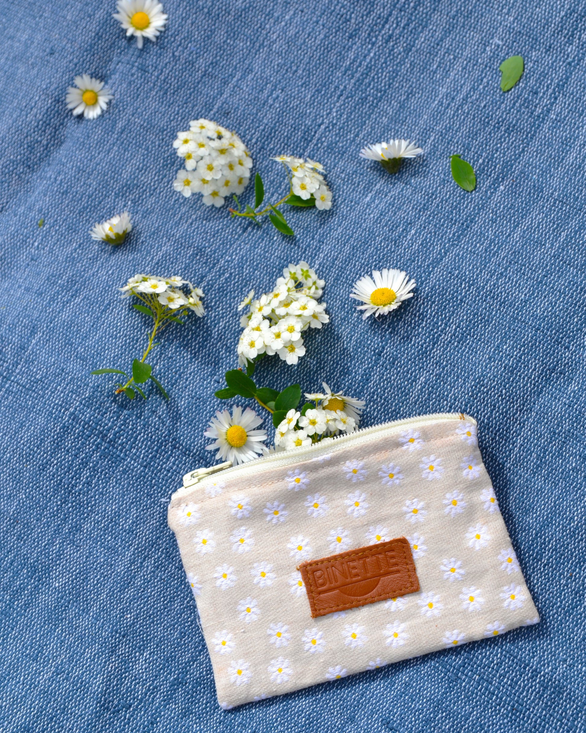 Cette photo met en lumière la polyvalence et le charme de la pochette Marguerite Beige. Son motif floral intemporel et sa doublure en coton beige en font un accessoire indispensable pour transporter vos essentiels avec style. 