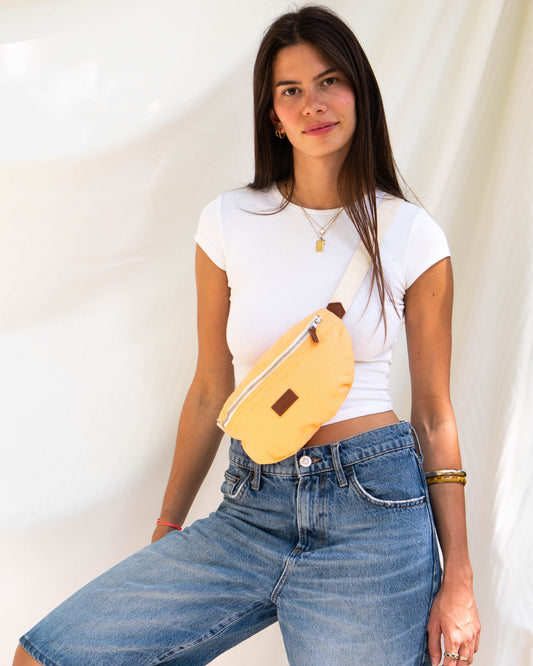 Jeune femme portant banane binette couleur pêche orange avec anse blanche réglable. 
Avec la Binette Pêche, la femme moderne peut exprimer son style avec aisance et assurance.