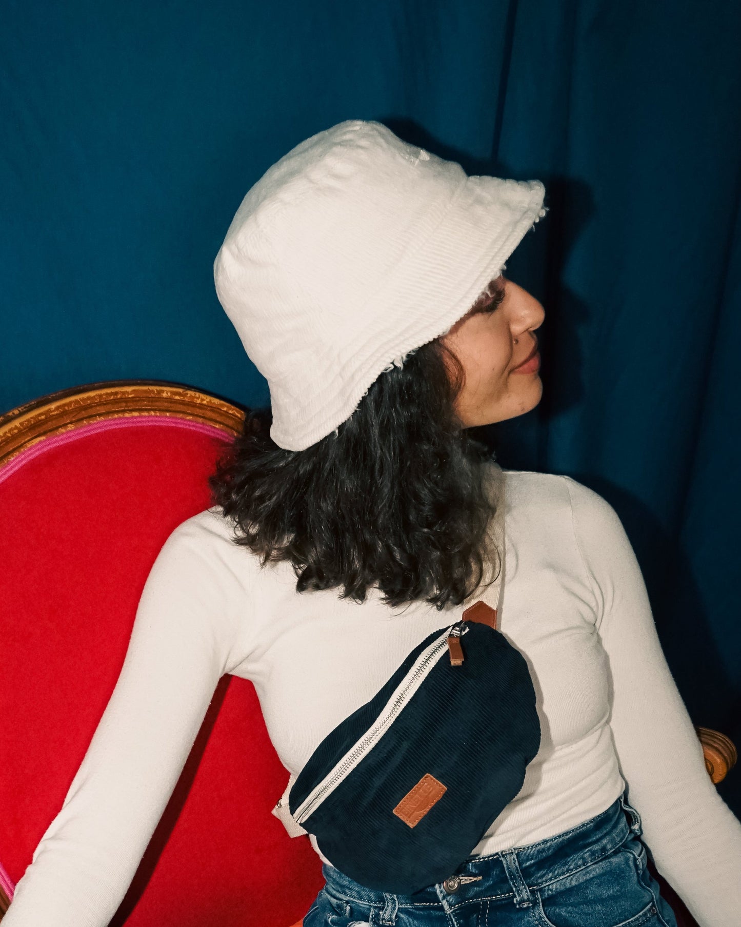 Modèle de profil portant le bob réversible Binette côté moumoute blanche, accompagné du sac banane en velours côtelé bleu marine. Une tenue écoresponsable en tissu upcyclé qui allie douceur, style et engagement pour une mode durable.