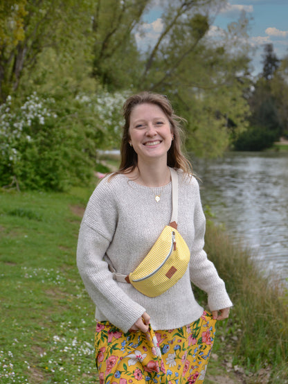 Jeune femme blonde portant un sac banane binette écoresponsable jaune motif vichy fait par une marque française.