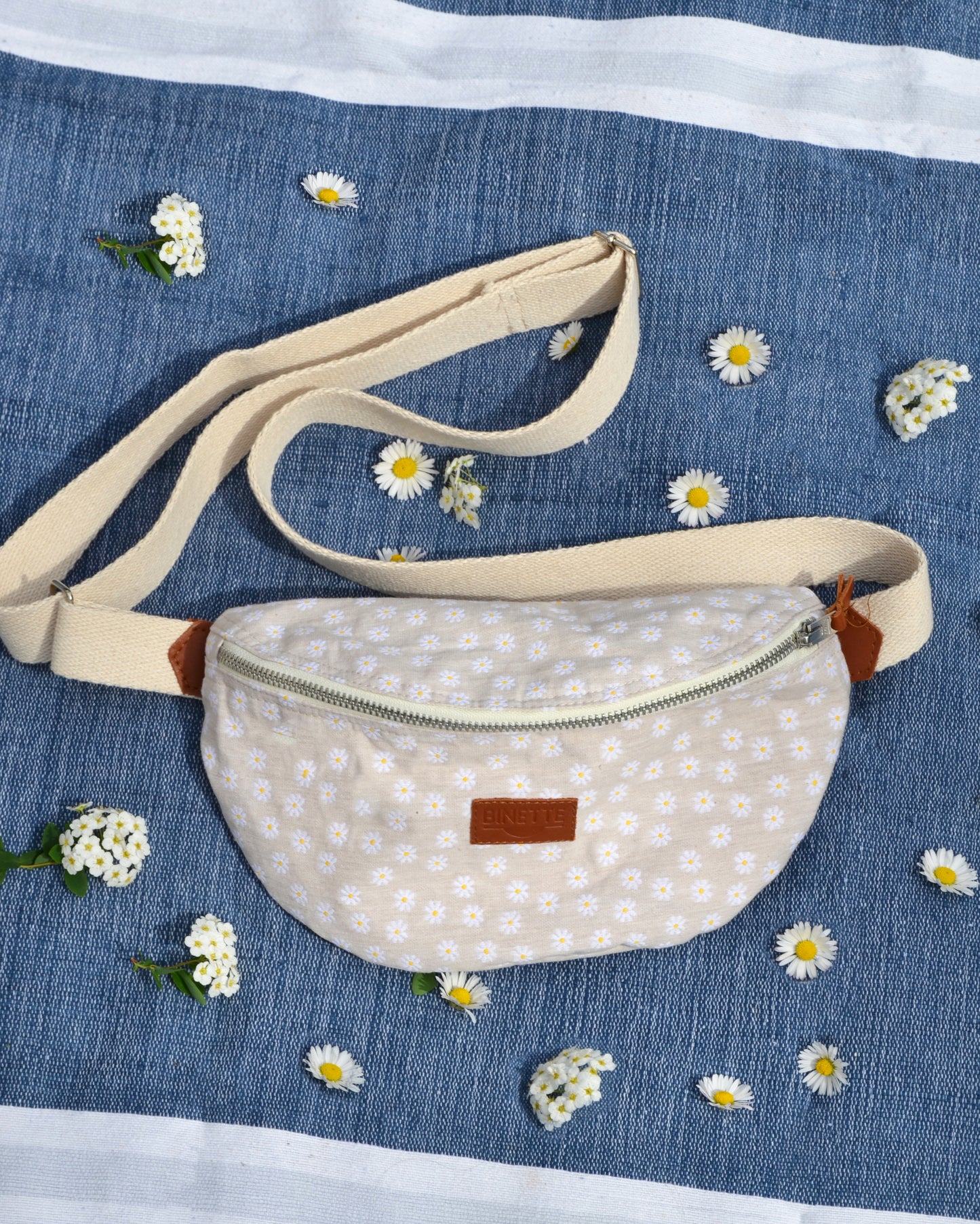 Cette photo en gros plan capture la beauté et la fonctionnalité du sac banane Marguerite Beige. Son motif floral délicat et sa doublure en coton beige ajoutent une touche de sophistication à ce sac polyvalent.