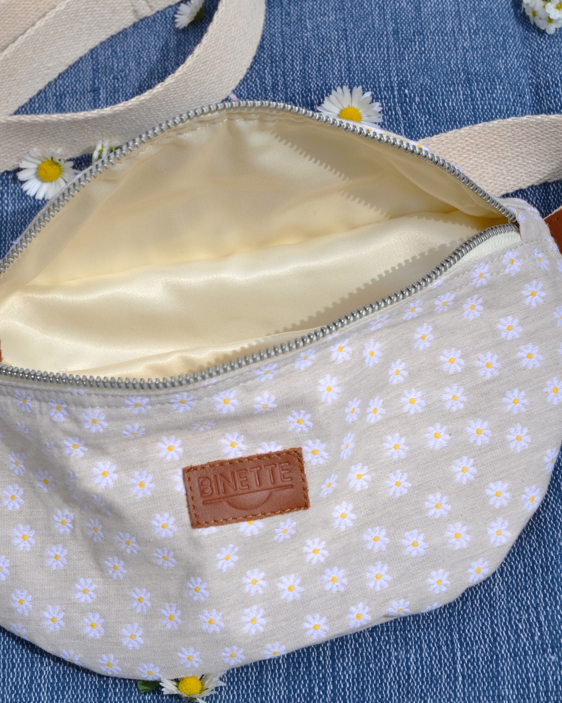 Découvrez le sac banane Marguerite Beige sous un nouvel angle avec cette photo captivante. Son motif floral élégant et sa doublure en coton beige offrent une combinaison parfaite de style et de praticité. Que ce soit pour une journée en ville ou une escapade en plein air, ce sac devient rapidement un compagnon de choix pour transporter vos essentiels avec aisance et élégance.