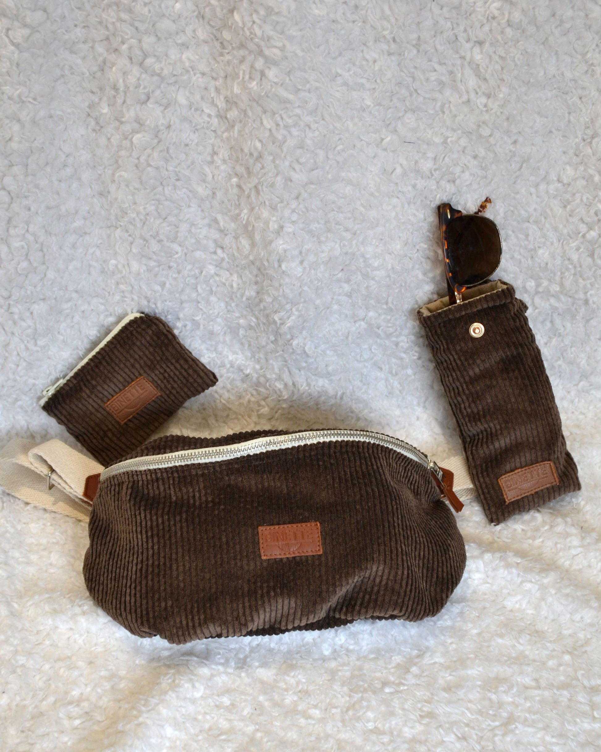 Pochette étui à lunette et banane Binette marron chocolat velours côtelé posés sur une moumoute blanche. Un pack écoresponsable en tissu upcyclé 