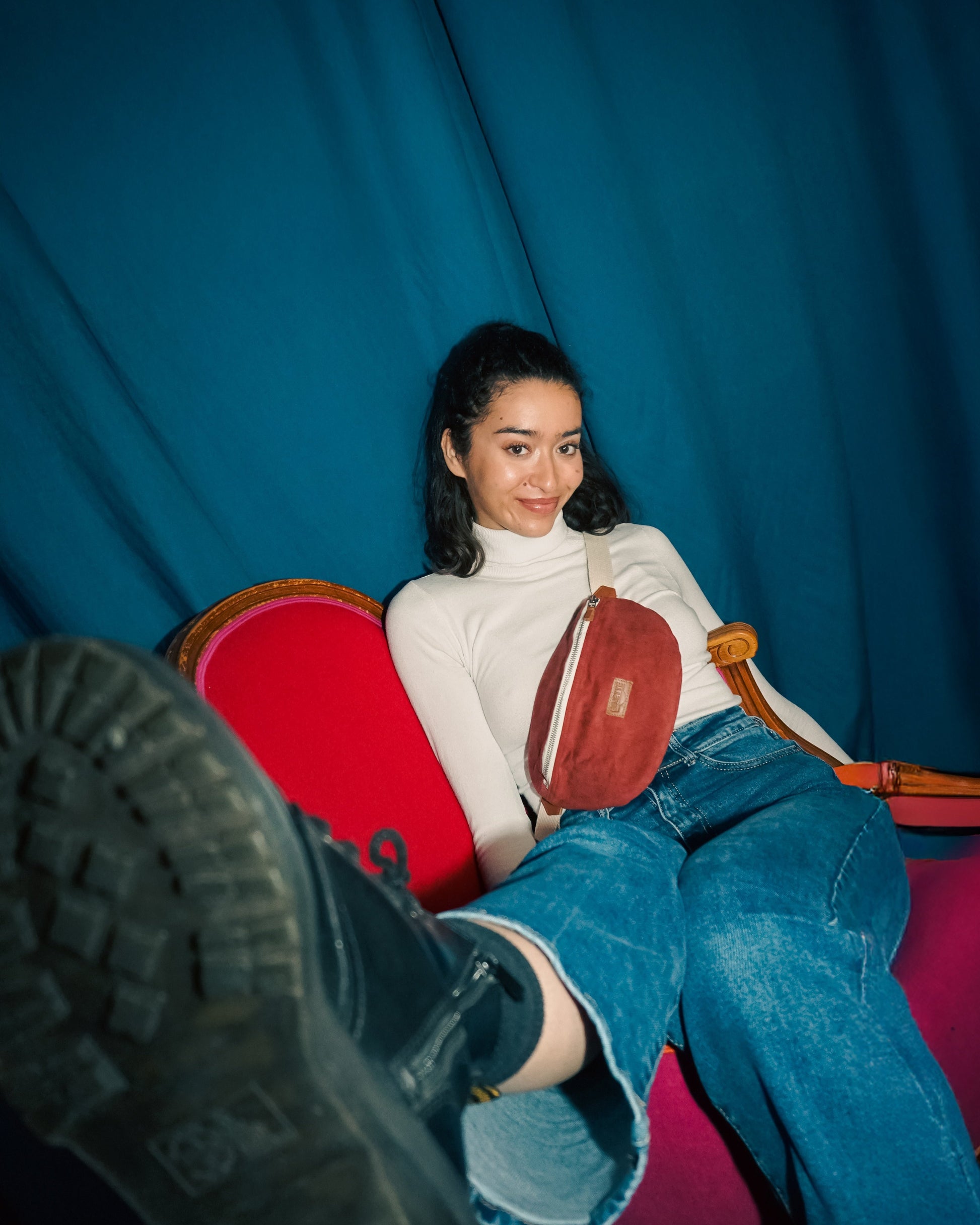 Modèle femme portant le sac banane Binette rouge en velours côtelé et fixant la caméra. 
Accessoire écoresponsable en tissu upcyclé qui allie douceur, style et engagement pour une mode durable.