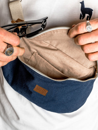 Jeune homme brun portant un Sac banane Binette écoresponsable fabriqué à partir de chutes de tissus dormants voués à être jetés ou brûlés bleu marine collection binette une marque française écoresponsable de sacs banane upcyclés et accessoires uniques et tendances luttant pour le gaspillage textile, en collaboration avec perus pour la collection de sacs banane fabriqué avec l'innovante matière Ecovero et coton recyclé