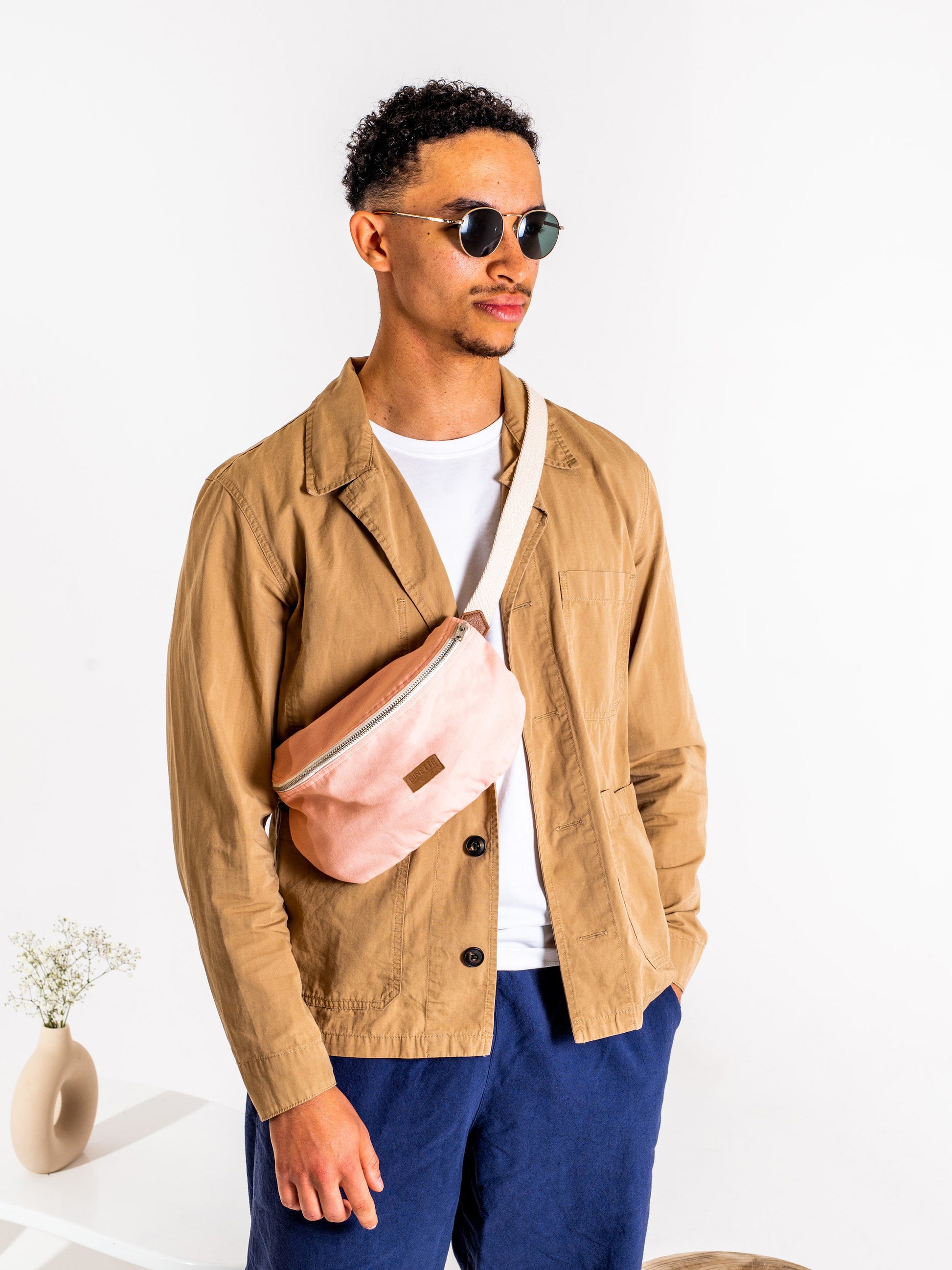 Jeune homme brun portant un Sac banane Binette upcyclé écoresponsable rose pâle collection binette x perus fabriqué à partir de chutes de tissus voués à être jetés ou brûlés et revalorisés par Binette la marque française écoresponsable de sacs banan eupcyclés et accessoires upcyclés ultra tendances, pratique, jolis, éthiques, durables, ecoresponsable, avec un faible impact environnemental, tout en luttant ocntre le gaspillage textile