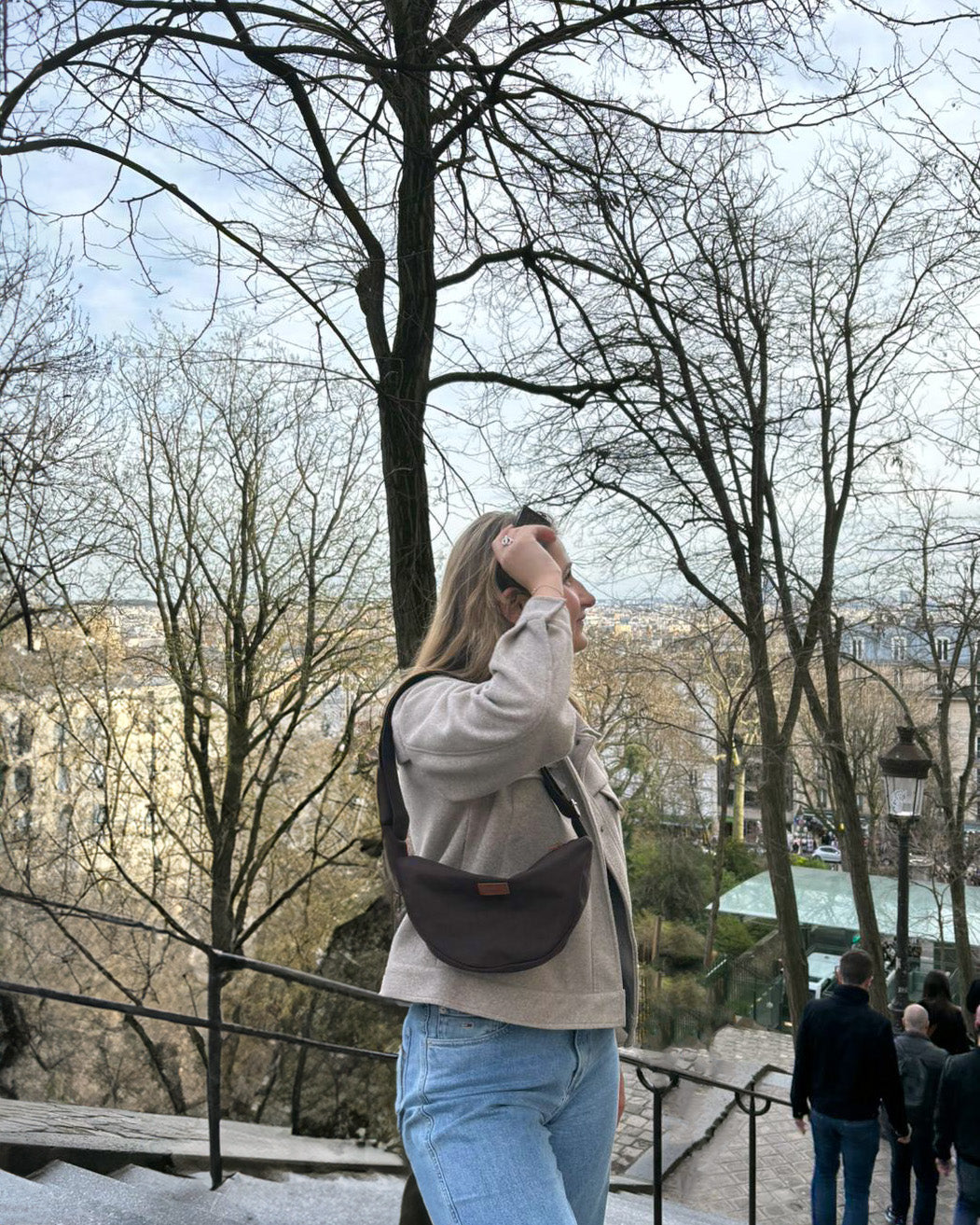 Dans cette scène ensoleillée, une femme radieuse porte le Sac Banane Demi-Lune en bandoulière avec aisance. Son sourire lumineux témoigne du confort et de la praticité de ce sac, qui lui permet de garder l'essentiel à portée de main tout en restant élégante. Le design épuré et l'histoire éthique derrière ce sac ajoutent une dimension de sens et de style à chaque tenue.