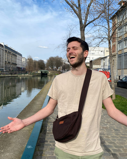 Cette image dynamique capture un homme confiant portant le Sac Banane Demi-Lune en bandoulière. Son attitude déterminée témoigne de la liberté de mouvement offerte par ce sac, qui lui permet de vaquer à ses occupations quotidiennes avec style et aisance. Le design éco-responsable et la fabrication 100% made in France ajoutent une touche de fierté à chaque tenue.