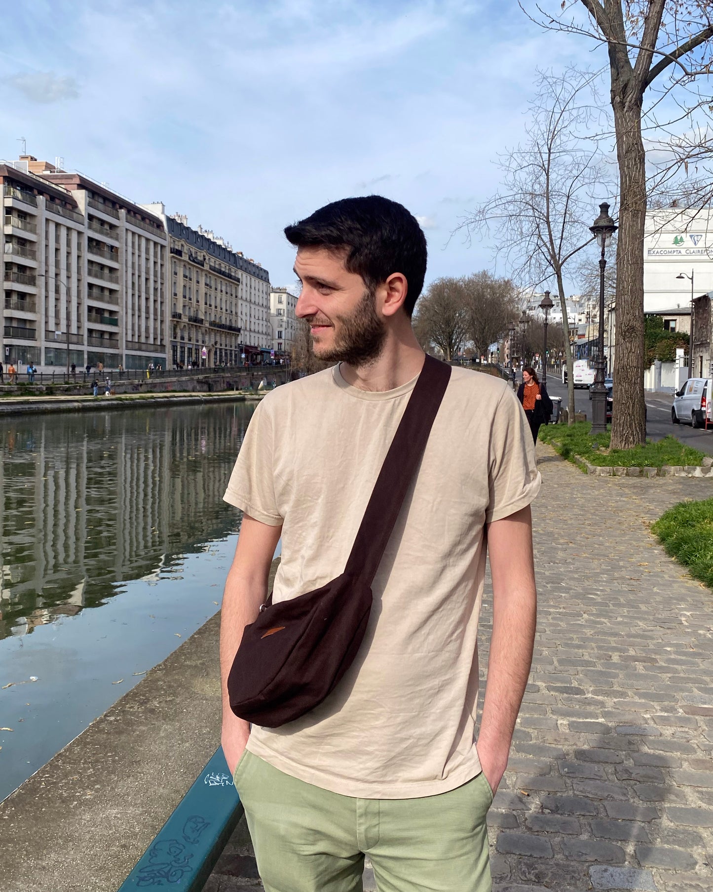 Dans cette scène urbaine, un homme décontracté arbore le Sac Banane Demi-Lune à la taille. Son sourire insouciant témoigne du confort et de la praticité de ce sac, qui lui permet de garder l'essentiel à portée de main tout en restant stylé. Avec son design épuré et son histoire éthique, ce sac devient un symbole de mode responsable et de style urbain.