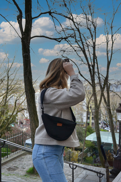 Dans cette scène urbaine, une femme affiche avec assurance le Sac Banane Demi-Lune, ajoutant une touche de style urbain à son look. Son attitude décontractée témoigne de la polyvalence de ce sac, qui peut être porté de manière décontractée en bandoulière ou à la taille pour un look plus tendance. Avec sa contenance généreuse et son design éco-responsable, ce sac devient rapidement un compagnon de choix pour toutes les aventures urbaines.