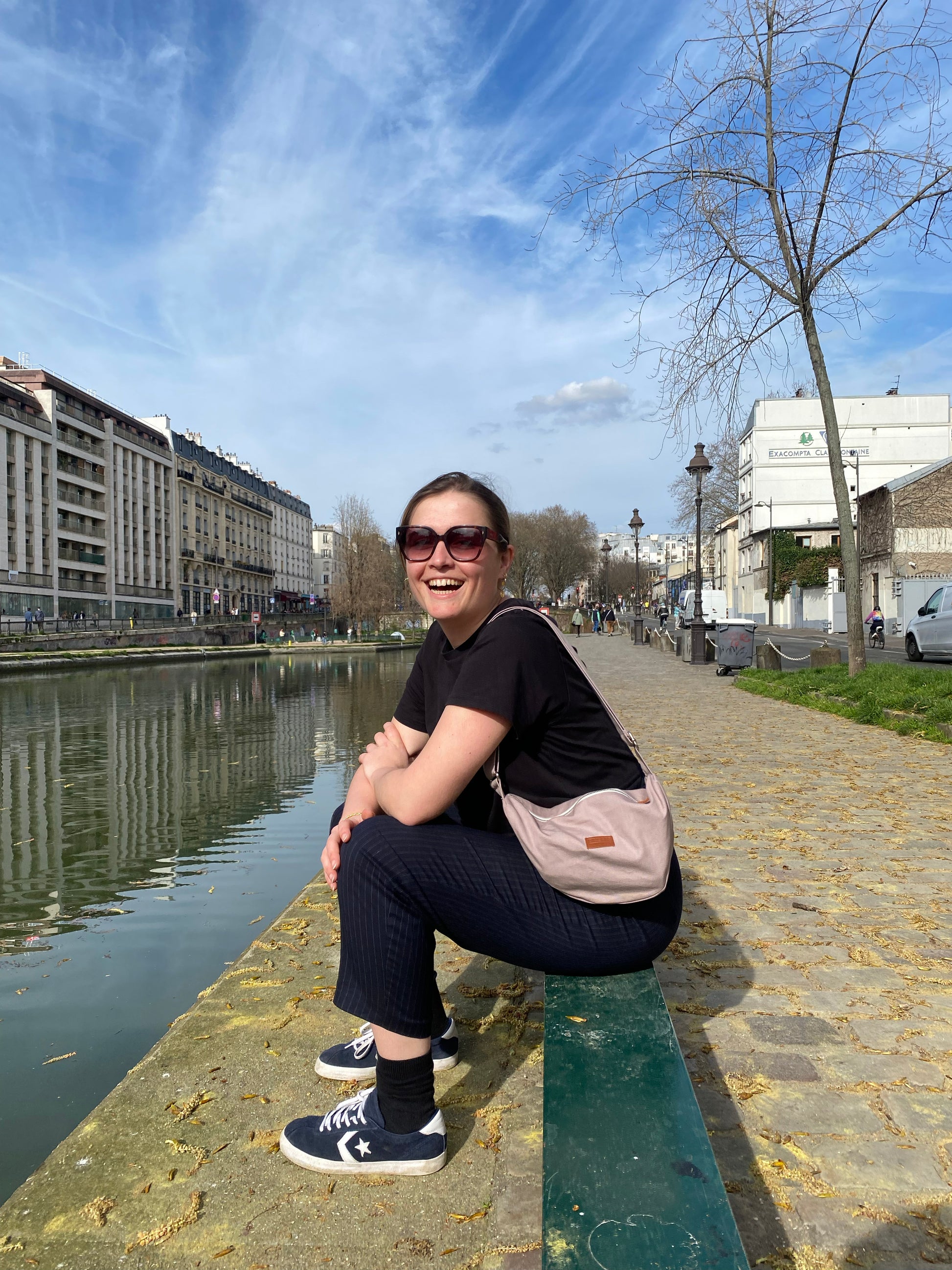 Dans cette scène urbaine, une femme affiche avec assurance le Sac Banane Demi-Lune gris lilas, ajoutant une touche de style décontracté à son look. Son attitude détendue témoigne de la polyvalence de ce sac, qui peut être porté de manière décontractée en bandoulière ou à la taille pour un look plus tendance. Avec sa contenance généreuse et son design éco-responsable, ce sac devient rapidement un compagnon de choix pour toutes les aventures urbaines.