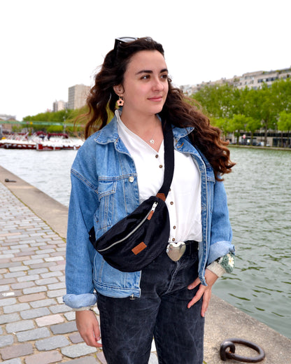 Dans cette scène ensoleillée, une femme élégante porte avec grâce la Binette Croco en bandoulière. Son allure confiante et son sourire rayonnant témoignent de l'aisance et de la praticité de ce sac, qui lui permet de garder tous ses essentiels à portée de main en toute élégance. Avec son total look noir et son effet crocodile subtil, la Binette Croco devient rapidement un accessoire incontournable pour celles qui recherchent style et fonctionnalité.