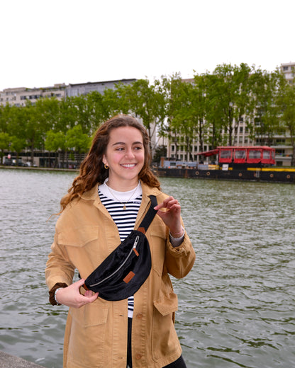 Dans cette scène ensoleillée, une femme élégante porte avec grâce la Binette Croco en bandoulière. Son allure confiante et son sourire rayonnant témoignent de l'aisance et de la praticité de ce sac, qui lui permet de garder tous ses essentiels à portée de main en toute élégance. Avec son total look noir et son effet crocodile subtil, la Binette Croco devient rapidement un accessoire incontournable pour celles qui recherchent style et fonctionnalité.