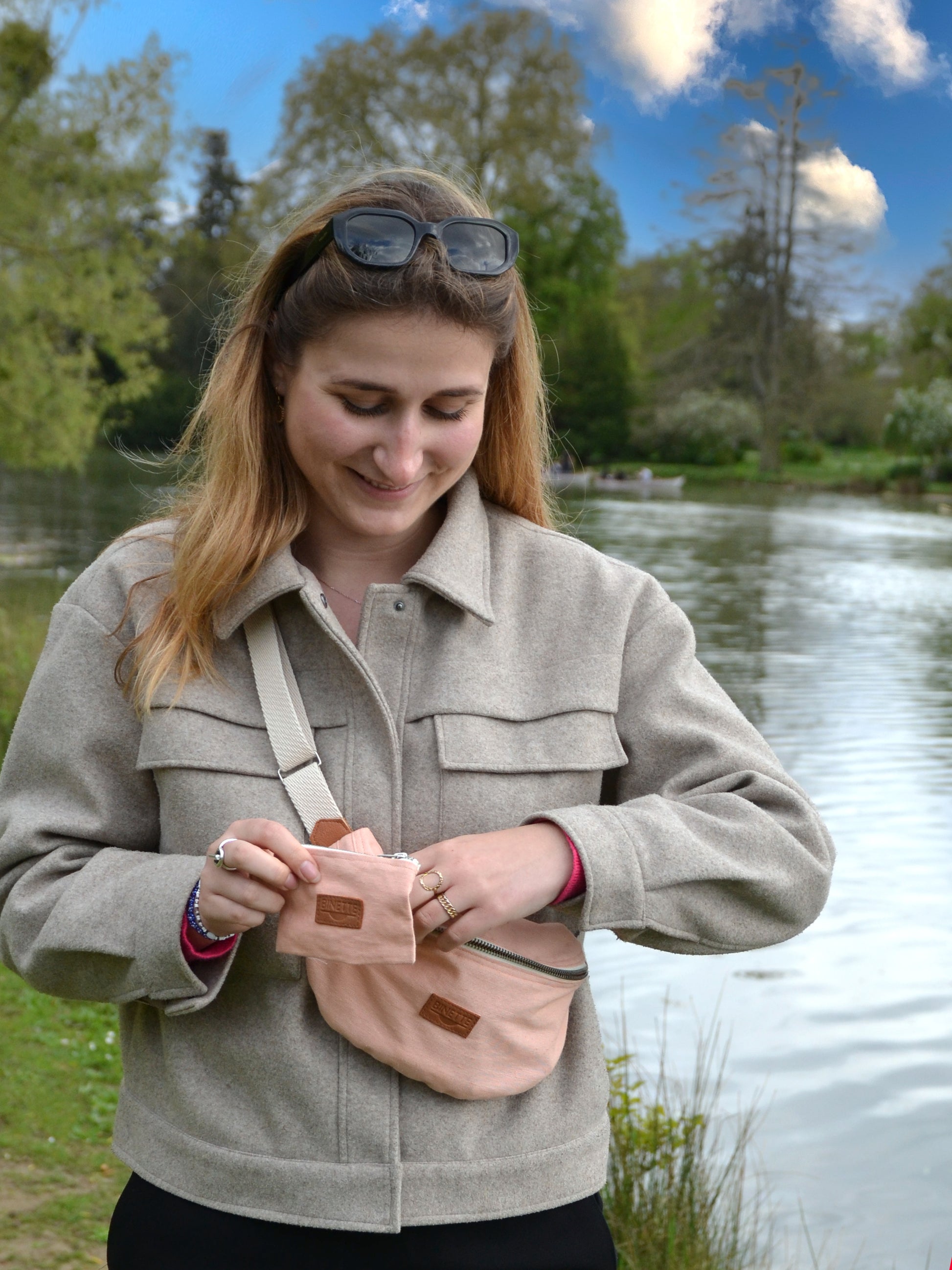 Jeune femme blonde portant un Sac bananae Binette Pivoine Rose pâle upcyclé  et une pochette fabriqués à partir de chutes de tissus dormants voués à être jetés ou brûlés et revalorisés par Binette la marque française de sacs banane et accessoires upcyclés pour en aire des sacs banane et accessoires pratiques, tendances, éthiques, ecoresponsable, durable, avec un impact environnemental faible et en luttant contre le gaspillage textile