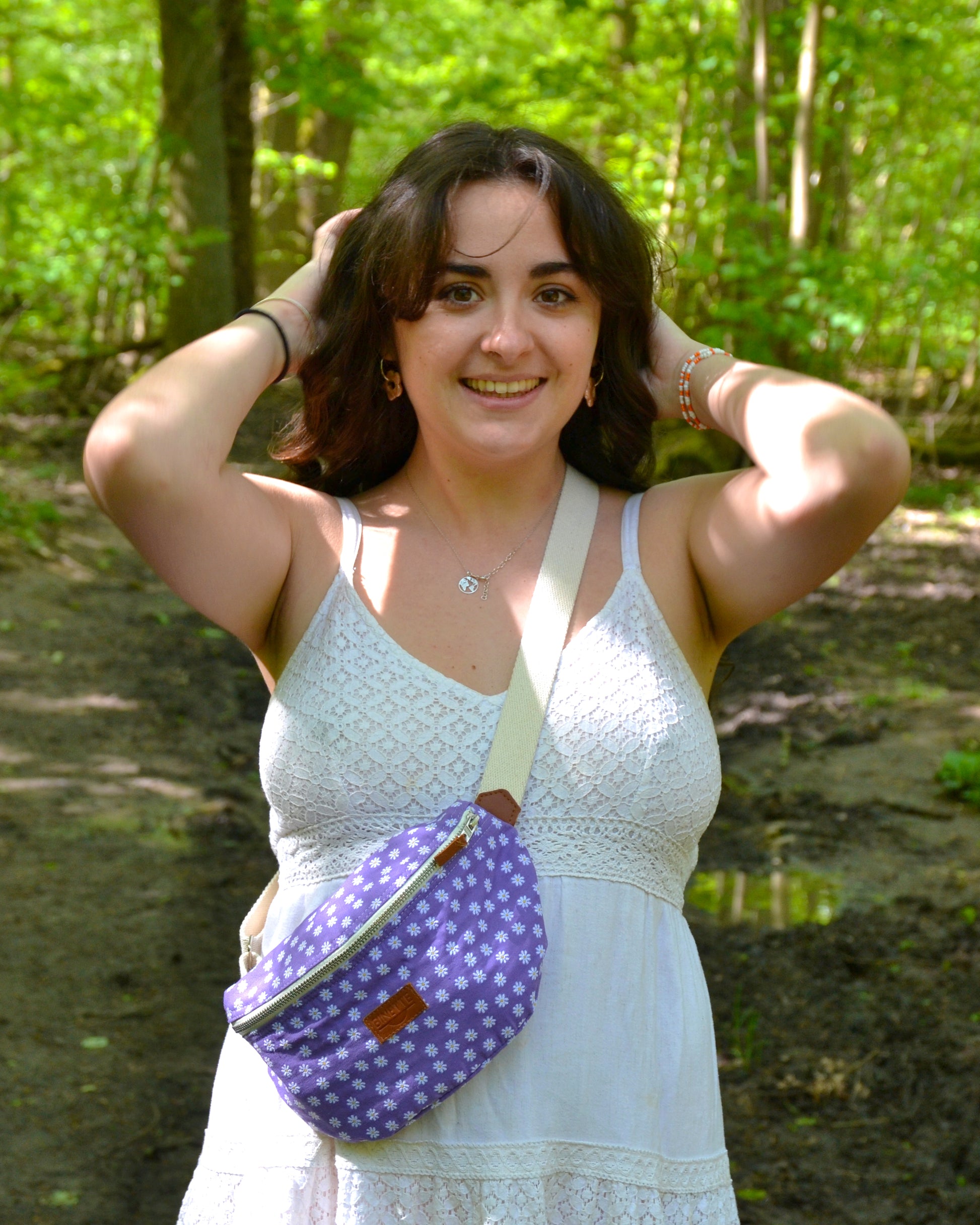 Dans cette scène ensoleillée, une femme radieuse porte la Binette Marguerite Violette en bandoulière, illustrant parfaitement la combinaison de liberté et d'élégance qu'offre ce sac. Son sourire lumineux témoigne du confort et de la praticité de cet accessoire, lui permettant de se déplacer en toute aisance tout en gardant l'essentiel à portée de main. La Binette Marguerite Violette devient ainsi le compagnon idéal pour une journée remplie d'aventures estivales.