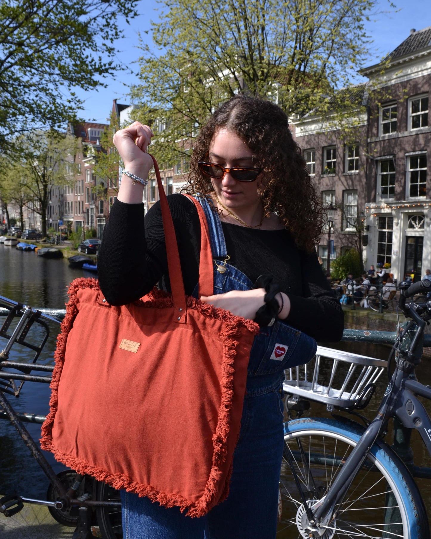 Capturant l'essence de l'élégance intemporelle, une femme porte le Sac Cabas Rouge Terracotta avec grâce. Son geste délicat et son regard déterminé reflètent la fusion parfaite entre style et fonctionnalité que ce sac incarne. Avec sa couleur rouge terracotta vibrante, il ajoute une touche de chaleur printanière à chaque tenue.