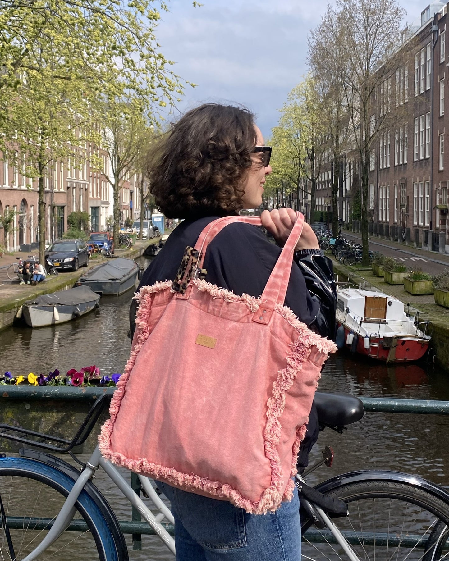 Cette première photo capture une femme élégante portant le sac cabas Rose Coeur lors d'une balade en ville. Son allure sophistiquée et son sourire radieux témoignent du charme vintage de ce sac, qui ajoute une touche de romantisme à sa tenue urbaine. Avec sa silhouette élégante et son style intemporel, le sac cabas Rose Coeur devient rapidement un incontournable pour celles qui recherchent l'alliance parfaite entre élégance et fonctionnalité.